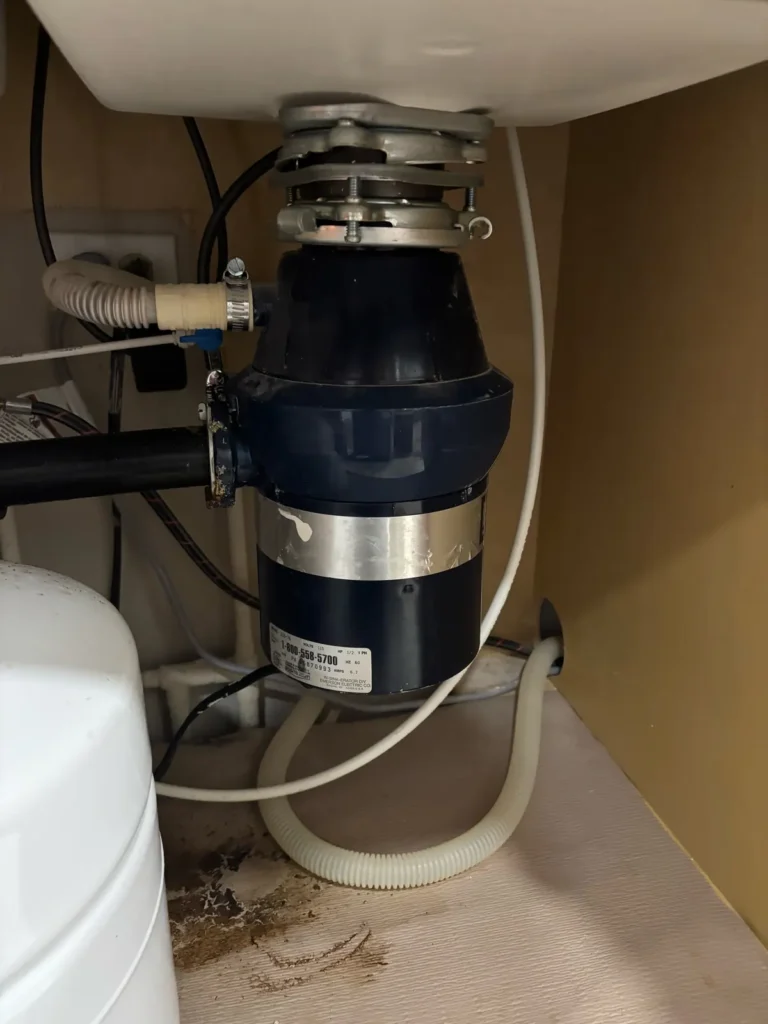 Old garbage disposal under a kitchen sink before replacement